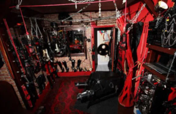 Cette image illustre l'équipement complet d'une salle de BDSM ou d'un donjon sexuel professionnel, offrant de nombreuses idées pour votre propre donjon DIY. Notez les crochets au plafond pour le bondage, essentiels pour un espace BDSM polyvalent. Les murs garnis de jouets et d'accessoires montrent l'importance du stockage dans un donjon bondage. Utilisez cette inspiration pour votre plan BDSM personnel, que vous souhaitiez créer une cave BDSM dédiée ou simplement intégrer des éléments comme une table BDSM ou un banc de bondage dans votre lieu BDSM.